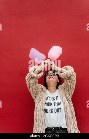 Lustiges Bild einer Frau, die ihre Arme mit zwei Zuckerwatte auf einem roten Hintergrund kreuzt. Speicherplatz kopieren Stockfoto