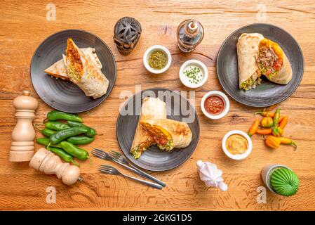 Bild von oben von mexikanischen Burritos mit Paprika, Saucen, frischem Pfeffer, schwarzem Schädel und Gabeln Stockfoto