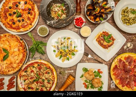 Bild von oben mit typisch italienischen Gerichten mit viel Basilikum, Pizza, Pasta, Gnocchi, Tomaten und Gemüse auf einem braunen Marmortisch Stockfoto