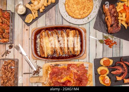 Beliebte spanische Tapas-Gerichte in einem Restaurant serviert. Puntillitas, spanische Omelette, gegrillte Rippchen mit roten Paprika, au Gratin Auberginen, gegrillter Oktop Stockfoto