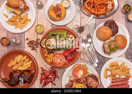 Mediterrane Gerichte mit Hamburgern, Süßkartoffelchips, gegrilltem Gemüse und Spargel, Hühnchen mit Grillsauce und Deluxe-Pommes Stockfoto