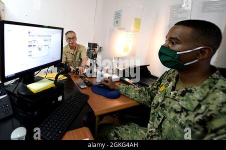 CAMP LEMONNIER, Dschibuti (14. April 2021)– U.S. Navy Master bei Arms Shay Riley aus Victorville, Calif, der derzeit einen vergasten Billet beim Personal Support Office (PSO) füllt, erstellt einen Ausweis für Charlie Hurt, Chief Engineer der US-Regierung Carl Brashear. Das Schiff wird für kurze Zeit im Hafen von Dschibuti angedockt, während die Besatzung administrative Unterstützung vom PSO-Büro im Camp Lemonnier erhält. Camp Lemonnier ist eine operationelle Einrichtung, die es US-amerikanischen, alliierten und Partnernationstruppen ermöglicht, dort zu sein, wo und wann sie gebraucht werden, um die Sicherheit in Europa, Afrika und im Südwesten zu gewährleisten Stockfoto