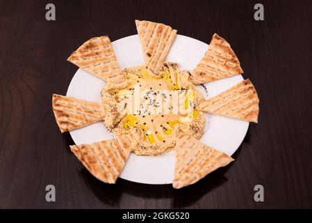 Kichererbsen-Hummus-Vorspeisen mit Olivenöl und ungesäuerten Brotscheiben zum Eintauchen auf einen Holztisch Stockfoto