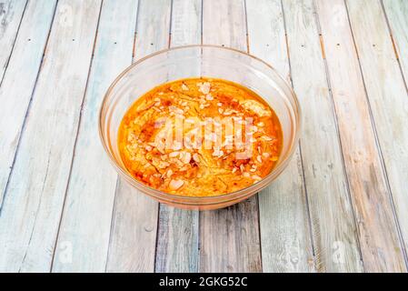 Riesige Schüssel mit Kichererbsen-Hummus mit Olivenöl, Paprika und Stücken leckerer roher Mandeln auf buntem Holzhintergrund Stockfoto