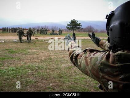 Sgt. Michael Cummings, UH-60 Blackhawk Helikopterreparator mit Firma C, 1. Bataillon, 168. General Support Aviation Bataillon, Washington Army National Guard, signalisiert Mitgliedern der Kosovo-Sicherheitskräfte, sich während einer medizinischen Evakuierungsübung aus der Luft auf dem KSF Training and Doctrine Command-Gelände in Ferizaj/Urosevac, Kosovo, am 14. April 2021 einem Flugzeug zu nähern. Cummings, der dem Regionalkommando Ost der Kosovo Force zugewiesen wurde, tauschten während der Schulung Best Practices für den Umgang mit Patienten aus. Stockfoto