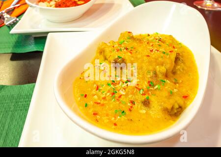 Gelbes Korma-Rezept mit fein gehacktem Gemüse und geschmortem Huhn in einer weißen Schüssel auf dem Tisch eines pakistanischen Restaurants Stockfoto