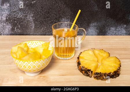 Ananasscheibe mit gehackter Haut, Schüssel mit geschälten Ananaswürfeln und Ananassaft in einer Glasschale Stockfoto