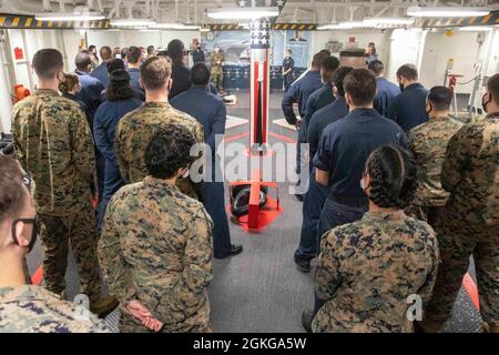 210415-N-TF178-1053 PAZIFISCHER OZEAN (15. April 2021) – US-Marineinfanteristen und Matrosen versammeln sich auf dem Schiff USS Makin Island (LHD 8) zur Enthüllung eines neuen Wandbildes. Die Makin Island Amphibious Ready Group und die 15. Marine Expeditionary Unit sind im Rahmen eines geplanten Einsatzes in der Region im 7. Flottengebiet der USA tätig. Als größte vorwärtseingesetzte Flotte der US-Marine operiert und interagiert die 7. Flotte routinemäßig mit 35 maritimen Nationen und führt Missionen durch, um eine freie und offene Indo-Pazifik-Region zu erhalten und zu schützen. Stockfoto