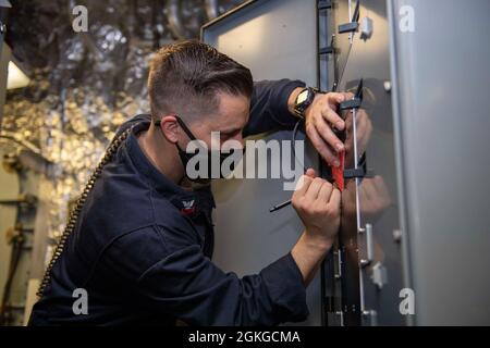 PAZIFIK (15. April 2021) Elektriker-Mate 1. Klasse Michael Critelli aus Rancho Cucamonga, Kalifornien, signiert während der Wartung an Bord des Litoral Combat Ship USS Charleston (LCS 18), April 15, einen Gefahrenschild. Charleston ist derzeit in der 3. US-Flotte tätig. Stockfoto