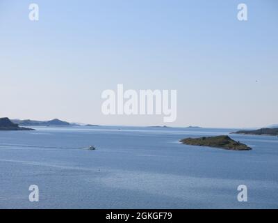 Winziges Boot in der Ferne, das sich über flache, ruhige Meere im Sound of Jura und einen verschwommenen Horizont mit den fernen Inseln der Inneren Hebriden bahnt. Stockfoto