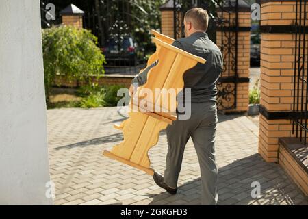 Der Typ trägt zwei Holzbänke. Der Mann zieht Objekte. Vorbereitung der Veranstaltung. Ein Mitarbeiter schleppt im Sommer Möbel. Stockfoto