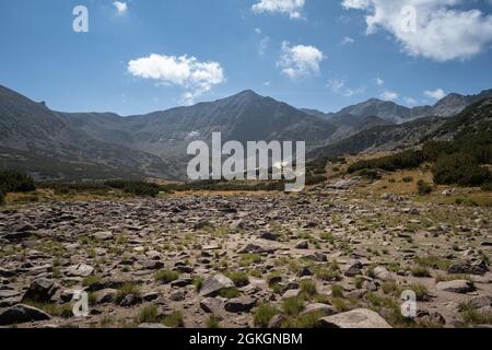 Im Vordergrund karge Felsen, Berghütte und beeindruckende ferne felsige Gipfel auf dem Wanderweg zum Musala Gipfel, Rila, Bulgarien Stockfoto