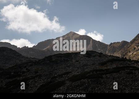 Goldenes, weiches Morgenlicht fällt auf den Gipfel des Musala auf dem Rila-Berg, im Vordergrund karge Felsen und entsättigt blauer Himmel Stockfoto