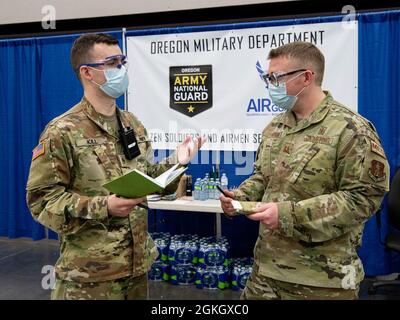 Stabsstab Der Nationalgarde Der Oregon-Armee Ryan Kill, der der Headquarters-Headquarters Company, dem 3. Bataillon, dem 116th Cavalry Regiment (links) und dem Oregon Air National Guard Capt. Daniel Vawter, dem 142nd Wing CERFP (rechts) zugeordnet ist, diskutiert den aktuellen Betriebsstatus der COVID-19-Massenimpfungsklinik im Oregon Convention Center, Portland, Oregon, Oregon, Oregon, USA, 19. April 2021. Am 6. April kündigte Präsident Joe Biden an, dass alle amerikanischen Erwachsenen bis zum heutigen Datum für einen Coronavirus-Impfstoff in Frage kommen würden, da Oregon Guardsmen seit ihrer Aktivierung mittlerweile über 300,000 Impfungen verabreicht haben. Stockfoto