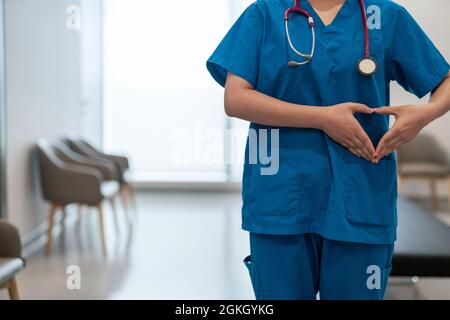 Flacher Fokus eines Arztes in Peelings, die eine Herzhandbewegung in einem Krankenhausflur machen Stockfoto