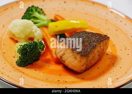 Gebackener Lachsfisch mit gedünstetem Gemüse, einschließlich Karotten, Blumenkohl, Brokkoli und Zucchini, gesundes Lebensmittelkonzept Stockfoto