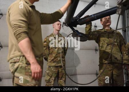 Personal Sgt. Justin Latham, Center, 341st Maintenance Group Quality Assurance Evaluator, inspiziert Senior Airman Dylan Funkhouser, Left, und Senior Airman Sean Moore, 341st Missile Maintenance Squadron Rakete Handling Technicians, während sie Geräte auf der Rückseite eines Transporter-Erektors montieren, um eine Raketenrollübertragung vorzubereiten 20. April 2021, In der Raketenabwicklungsanlage auf der Luftwaffenbasis Malmstrom, Mtn., wird das abgebildete Kabel um den Ankerpunkt geschraubt und an einem Fördergurtsystem innerhalb der T.E. befestigt, das die Rakete von Fahrzeug zu Fahrzeug bewegt. Stockfoto