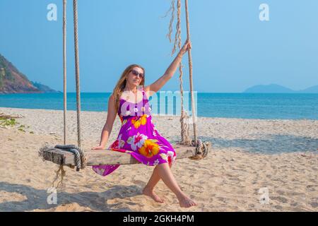 Junge Frau schwingt auf einer Schaukel, die an einer Palme am Meer hängt. Reisen und Tourismus in die tropischen Länder Asiens. Stockfoto