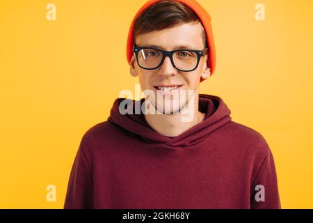 Porträt eines gutaussehenden Mannes mit orangefarbenem Hut, rotem Pullover und Brille auf gelbem Hintergrund, lächelnd, herbstliche Stimmung Stockfoto