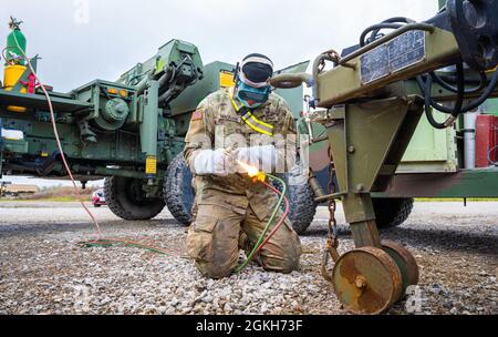 SPC der US-Armee. Phoenix Macrabie, ein Mechaniker mit Rädern, der der Forward Support Company 204th Engineer Battalion, 153rd Truppenkommando Brigade, 53. Truppenkommando, zugeordnet ist, schweißt, um eine Kette mit Sicherheitshaken im Regional Support Camp Panther, North Vernon, Ind., 21. April 2021 zu reparieren. Hinter Macrabie steckt Sgt. Melinda Farnham, eine Mechanikerin auf Rädern, steht für Sicherheit zur Verfügung. Soldaten der Nationalgarde von NY unterstützen andere Bataillone der Nationalgarde während der Guardian Response Übung 21 in Indiana operativ und logistisch. Stockfoto