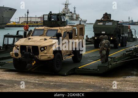 U.S. Marineinfanteristen mit 9. Ingenieur unterstützen Bataillon und Navy Seabees mit bewegtem Naval-Baubataillon 4 entlasten ein gemeinsames leichtes taktisches Fahrzeug und ein High Mobility Artillery Rocket System mit 12. Marines, 3d Marine Division, von einer verbesserten Bandbrücke während der Übung Pacific Pioneer, Naha Port, 21. April 2021. Pacific Pioneer diente als 9. ESB Marine Corps Combat Readiness Evaluation sowie als Gelegenheit, die Fähigkeit zu demonstrieren, Expeditions-Advanced Basen mit überlebensfähigen Kraftschutz aufrechtzuerhalten, Marine-Integration zu üben und Langstreckenfeuern und Ta zu positionieren Stockfoto