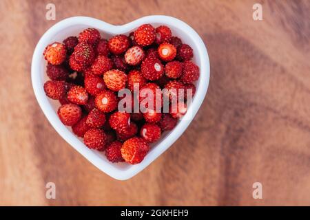 Herzförmige Schüssel voll von reifen roten saftigen wilden Erdbeeren auf Holz Hintergrund. Draufsicht. Speicherplatz kopieren Stockfoto