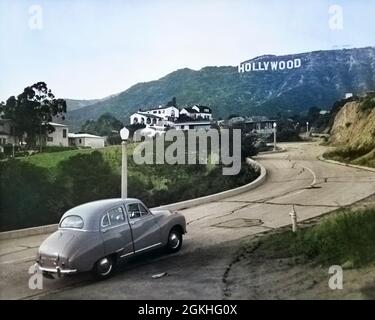 1950ER JAHRE AUSTIN AUTO FÄHRT STRASSE IN DEN HOLLYWOOD HILLS MIT HOLLYWOOD-ZEICHEN IN DER ENTFERNUNG LOS ANGELES KALIFORNIEN USA - Q53014C CPC001 HARS KOMMUNIZIEREN HOLLYWOOD HILLS HOLLYWOOD-ZEICHEN STRASSEN 1923 WAHRZEICHEN LOS ANGELES ALTMODISCH Stockfoto