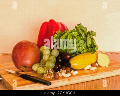 Rohe gesunde Lebensmittel auf einem Holzteller angeordnet. Gesunde Rohkost in Form von rotem Pfeffer, rotem Apfel, Früchten, Salatherz, Nüssen, Weiße Trauben, Banane. Stockfoto