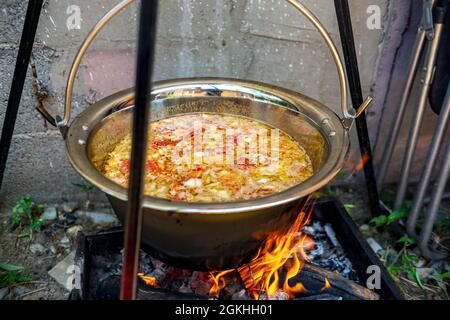Topf mit Gemüsekessel über offenem Feuer, Zubereitung von Eintopf auf Holzgrill, Kochen im Freien Stockfoto
