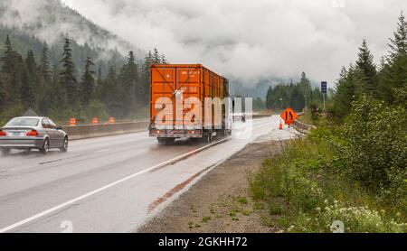 LKW und andere Autos fahren bei Regen und Waldbränden entlang der Autobahn durch den Wald. Stockfoto