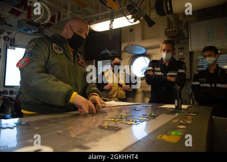 Französische Marine ADM hinten. Eric Malbrunot, Mitte rechts, stellvertretender Leiter der Marineoperationen für Pläne und Programme, erhält einen Brief von LT. Christopher Jones, links, USS Gerald R. Ford's (CVN 78) Aircraft Handling Officer, über das Flugdeck-Design des Schiffes, in Ford's Flight Deck Control während einer Schiffstour, 23. April 2021. Die leitende Leitung der französischen Rüstungsbeschaffungsagentur (DGA) besuchte Ford, um das elektromagnetische Flugzeugstartsystem (EMALS) und das Advanced Arresting Gear (AAG) in Betrieb zu sehen, um Frankreich zu ermöglichen, das Design der zukünftigen französischen Fluggesellschaft zu verfeinern. Beschaffung von EMALS und AAG durch Stockfoto