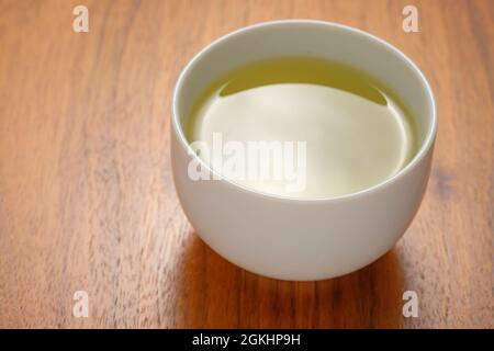 Gesunder grüner Tee, serviert in einer weißen, minimalistischen Tasse aus Keramik auf einem Holztisch Stockfoto