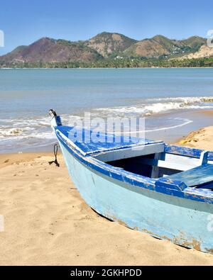 Traditionelles karibisches Fischerboot an einem Sandstrand mit Hügeln in der Ferne. ANASCO Beach, Puerto Rico, USA. Speicherplatz kopieren. Vertikales Format. Stockfoto