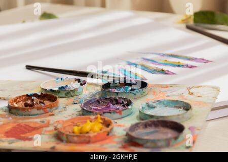 Palette mit Wasserfarbe auf einem dünnen Pinsel gemischt, Arbeitswerkzeuge, Hintergrund ein Arbeitsbuch mit einer künstlerischen Zeichnung, Hobby, kreativen Lebensstil im Studio Stockfoto
