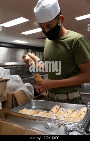 PAZIFIK (27. April 2021) U.S. Marine Corps Lance CPL. Marco Diaz, ein Elektriker, der dem 1. Kampfingenieur-Bataillon der 11. Marine Expeditionary Unit (MEU) aus Los Angeles zugewiesen wurde, bereitet Enchiladas in der Galeere auf dem amphibischen Angriffsschiff USS Essex (LHD 2) vor, April 27. Matrosen und Marineinfanteristen der Amphibious Ready Group (ARG) von Essex und der 11. MEU führen vor der Küste Südkaliforniens Routinetraining durch. Zusammen werden die 11. Marine Expeditionary Unit (MEU), das amphibische Squadron (PHIBRON) 1 und Schiffe als ARG bezeichnet. Stockfoto