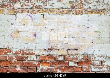 Raue verputzte Ziegelwand mit Rissen. Bunte Textur, abblätternder Putz. Vintage-Hintergrund Stockfoto