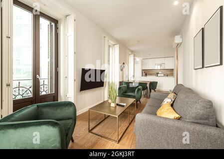 Wohnzimmer mit Fernseher in einer Ferienwohnung mit grünen Samtsofas, Klimaanlage an der Wand und großen Fenstern Stockfoto
