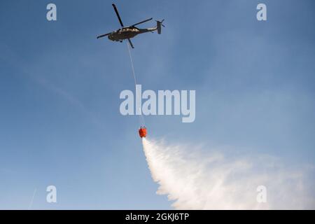 Ein UH-60 Blackhawk tropft während eines vorgeschriebenen Burn- und Eimer-Drop-Trainings am 29. April 2021 in Camp Guernseys North Training Area Wasser auf die Brandlinie. Stockfoto