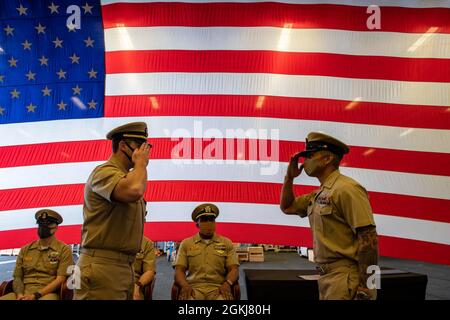 SASEBO, Japan (30. April 2021) Ensign Chris Colliver, links, erhält seinen ersten Gruß von Master Chief Fire Controlman Robinson O’Connor während seiner Inbetriebnahmezeremonie in der Hangarbucht des vorwärts eingesetzten amphibischen Angriffsschiffs USS America (LHA 6). Amerika, das führende Schiff der America Amphibious Ready Group, ist im Verantwortungsbereich der 7. Flotte der USA tätig, um die Interoperabilität mit Verbündeten und Partnern zu verbessern und als einsatzbereite Einsatztruppe für den Frieden und die Stabilität in der Region Indo-Pazifik zu dienen. Stockfoto