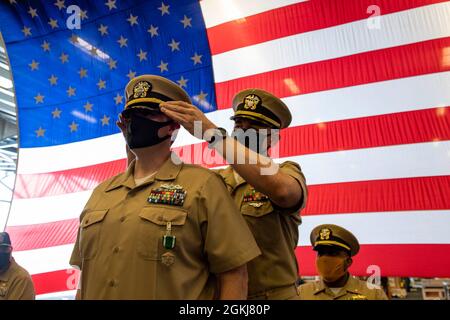 SASEBO, Japan (30. April 2021) Ensign Chris Colliver, ehemals Chief Electronics Technician, der dem im Vorlauf eingesetzten amphibischen Angriffsschiff USS America (LHA 6) zugewiesen wurde, erhält während seiner Inbetriebnahmezeremonie in der Hangarbucht des Schiffes die Abdeckung seines Offiziers. Amerika, das führende Schiff der America Amphibious Ready Group, ist im Verantwortungsbereich der 7. Flotte der USA tätig, um die Interoperabilität mit Verbündeten und Partnern zu verbessern und als einsatzbereite Einsatztruppe für den Frieden und die Stabilität in der Region Indo-Pazifik zu dienen. Stockfoto