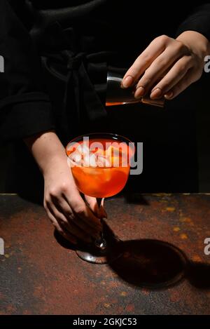 Weibliche Barkeeperin, die auf dunklem Hintergrund einen leckeren aperol Spritz Cocktail zubereitet, aus der Nähe Stockfoto