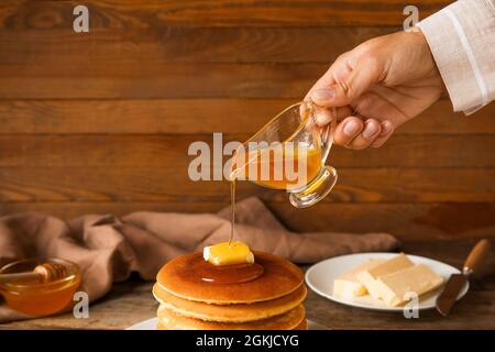 Frau gießt Honig auf leckere Pfannkuchen auf Holzhintergrund Stockfoto