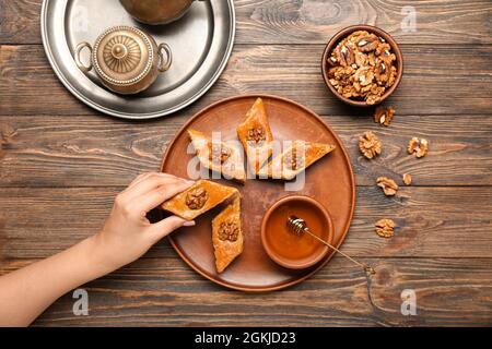 Frau nimmt leckere Baklava von Platte auf Holzhintergrund Stockfoto