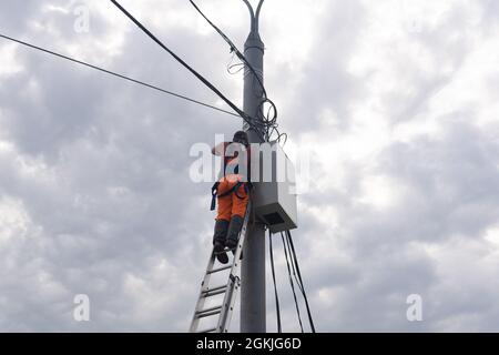 Perm, Russland - 25. August 2021: Elektriker oder Telekommunikationsleiter arbeitet an der Verlegung eines Kabels an der Spitze eines Telefonpols Stockfoto