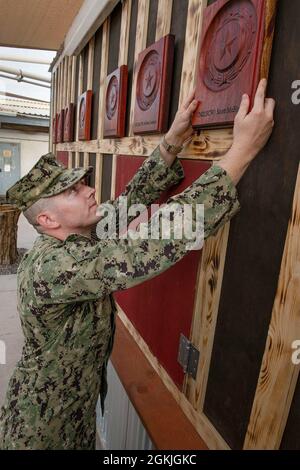 CAMP LEMONNIER, Dschibuti (4. Mai 2021) der US-Marine-Stahlarbeiter Dylan Patchack der 1. Klasse aus McEwen, Tennessee, der dem Marine Mobile Construction Bataillon (NMCB) 14, Abteilung 1, zugewiesen wurde, legt eine Gedenktafel an die renovierte Old Cantina His Team für eine Gedenkfeier auf dem Stützpunkt am 4. Mai 2021. Die Struktur wurde sieben NMCB 14 Seabees gewidmet, die vom 30. April 2004 bis zum 2. Mai 2004 im Irak getötet wurden. Seabee ist ein Spitzname, der von den ersten Buchstaben 'C und B' aus den Worten Baubataillon stammt. Der Geist der Seabee „kann“, symbolisiert die Naval Construction Force Sailo Stockfoto