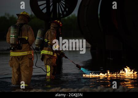 Zwei Feuerwehrmänner, die der 7. Zivilingenieursstaffel zugeordnet sind, entzünden während einer nächtlichen Feuerausbildung auf der Dyess Air Force Base, Texas, am 4. Mai 2021 ein Feuer. Während der Brandschulung wurde ein brennbares Gas auf der Wasseroberfläche entzündet, um die Ansammlung und Verbrennung von Strahlkraftstoff um ein Flugzeug herum zu simulieren. Stockfoto