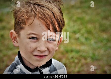 Kaukasischer Junge, der am Spieltag für seine Schwester auf einem sonnigen Fußballfeld die Kamera anschaut Stockfoto