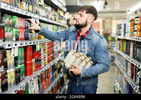 Interessierter junger Mann, der im Lebensmittelgeschäft Einkäufe tätigt und Bier aus der Dose kauft Stockfoto