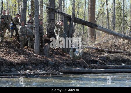 Sgt. Randall Henrion der 1. Klasse zieht sich über das Wasserhindernis, während der Rest seines Zuges ihn anfeuert. Soldaten einer Truppe, der 1. Staffel (Airborne), des 40. Kavallerieregiments nutzten einen schönen Frühlingstag, um Flusskreuzungstechniken über Ship Creek auf der Joint Base Elmendorf-Richardson am 13. Mai 2021 zu üben. (Foto der Armee/John Pennell) Stockfoto