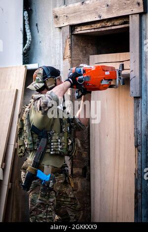 OKINAWA, Japan – Ein Grüner Beret mit 1. Bataillon, 1. Special Forces Group (Airborne), nutzt eine Stromsäge, um während der direkten Einsatztrainings in Camp Hansen, Okinawa, Japan, im Mai 2021 ein Gebäude zu durchbrechen. Direkte Eingreifaktionen sind kurzzeiige Streiks, die verwendet werden, um bestimmte Personen oder Material zu beschlagnahmen, zu zerstören, zu erfassen, zurückzugewinnen oder Schaden zuzufügen. Stockfoto